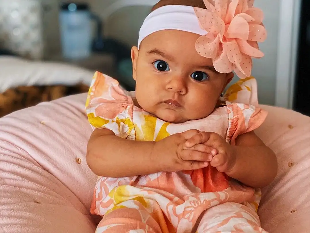 Face, Cheek, Skin, Head, Hairstyle, Eyes, Facial Expression, Comfort, Dress, Baby & Toddler Clothing, Orange, Baby, Pink, Iris, Finger, Toddler, Happy, Sitting, Peach, Person, Headwear