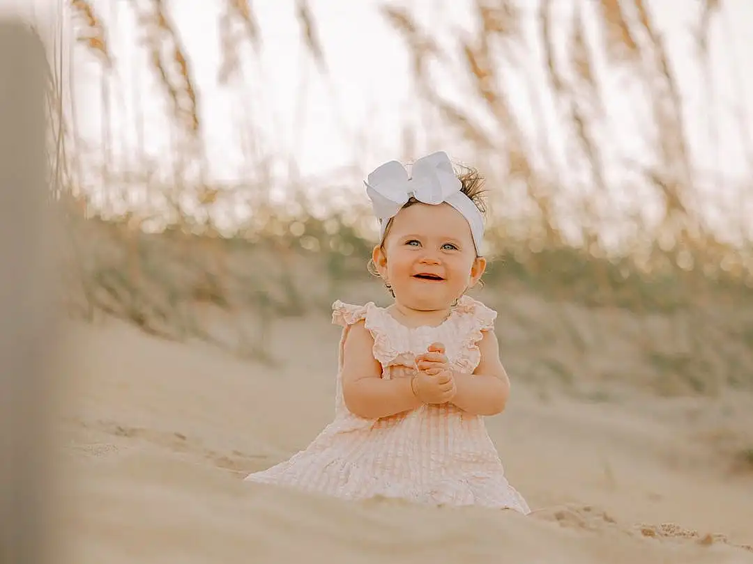 Eyes, Smile, Flash Photography, Sleeve, Dress, Baby & Toddler Clothing, Happy, Toddler, Headpiece, Baby, Embellishment, People In Nature, Grass, Hair Accessory, Fashion Accessory, Sky, Child, Hat, Headband, Sitting, Person, Joy, Headwear