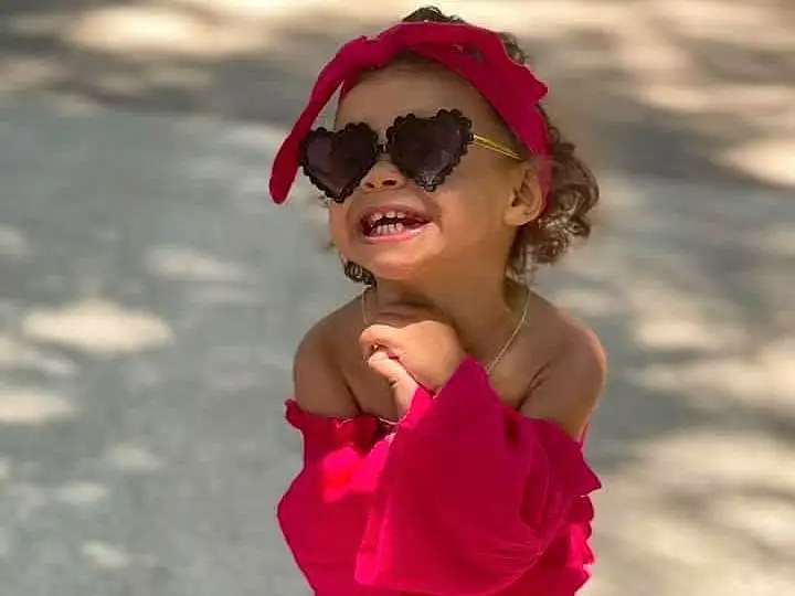 Face, Glasses, Lip, Smile, Goggles, Vision Care, Sunglasses, Dress, Sleeve, One-piece Garment, Happy, Eyewear, Gesture, Pink, Hat, Toddler, Day Dress, Street Fashion, Waist, Recreation, Person, Headwear