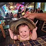Head, Photograph, Smile, Hat, Chair, Wood, Fun, Sun Hat, Leisure, Recreation, Event, Indoor Games And Sports, Pattern, Cooking, Design, Child, Finger Food, Person, Joy, Blurred