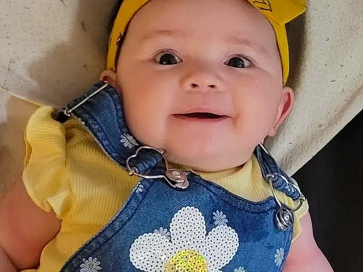 Face, Cheek, Skin, Lip, Smile, Eyes, Facial Expression, Baby & Toddler Clothing, Sleeve, Iris, Yellow, Baby, Happy, Flower, Headgear, Toddler, Baby Products, Child, T-shirt, Pattern, Person, Headwear