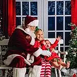 Smile, Photograph, Leg, Window, Hat, Santa Claus, Plant, Red, Lap, Christmas Tree, Curtain, Toddler, People, Fun, Happy, Tree, Christmas Decoration, Christmas Ornament, Event, Person, Joy, Headwear