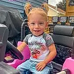 Skin, Smile, Hairstyle, Vehicle, Vroom Vroom, Facial Expression, Automotive Design, Shorts, Pink, Automotive Exterior, Toddler, Leisure, Lap, Steering Wheel, Fun, Auto Part, Vehicle Door, Car Seat, Car Seat Cover, Person, Joy