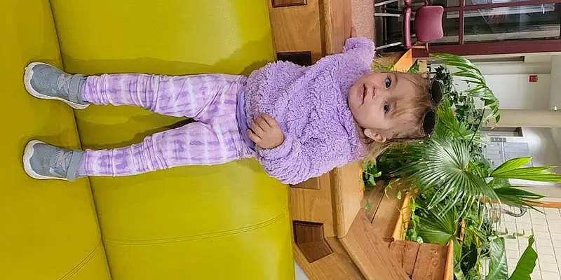 Smile, Purple, Plant, Yellow, Violet, Terrestrial Plant, Baby, Leisure, Toddler, Baby & Toddler Clothing, Fun, Magenta, Child, Comfort, Hat, Event, Happy, Room, Couch, Human Leg, Person