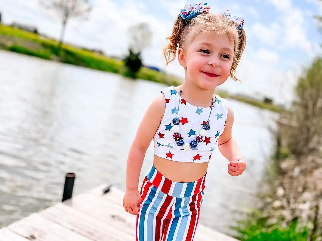 Clothing, Smile, Water, Sky, Plant, Cloud, People In Nature, Tree, Happy, Standing, Dress, Wood, Baby & Toddler Clothing, Leisure, Toddler, Street Fashion, Lake, Grass, Child, Electric Blue, Person, Joy