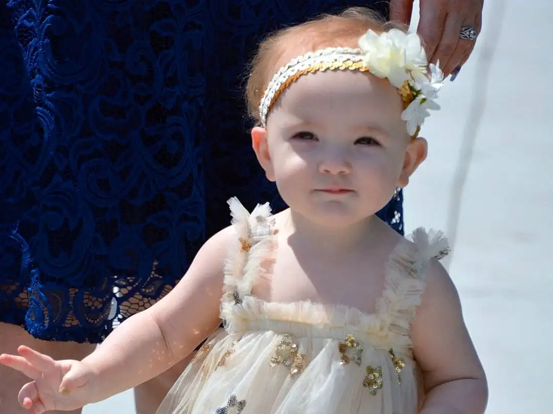Face, Skin, Head, Hairstyle, Arm, Shoulder, Eyes, Dress, Embellishment, Iris, Gesture, Happy, Petal, Headpiece, Day Dress, Bridal Clothing, Toddler, Baby & Toddler Clothing, Fashion Design, Gown, Person, Headwear