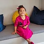 Clothing, Hair, Hand, Hairstyle, Shoulder, Purple, Dress, Human Body, Smile, Comfort, Baby & Toddler Clothing, Sleeve, Pink, Happy, Toddler, Magenta, Couch, Thigh, Fashion Design, Person, Joy