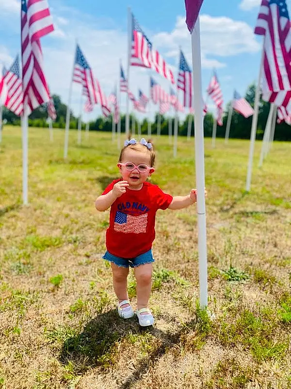 Cloud, Sky, Plant, Flag, Smile, Shorts, White, People In Nature, Flag Of The United States, Natural Environment, Grass, Happy, Grassland, Toddler, Tree, Flag Day (usa), Baby & Toddler Clothing, Fun, Leisure, Person