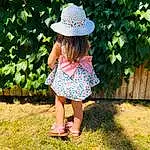 Footwear, Plant, Hat, Dress, People In Nature, Sun Hat, Baby & Toddler Clothing, Headgear, Grass, Toddler, Groundcover, Day Dress, Recreation, Grassland, Meadow, Pattern, Happy, Leisure, Fun